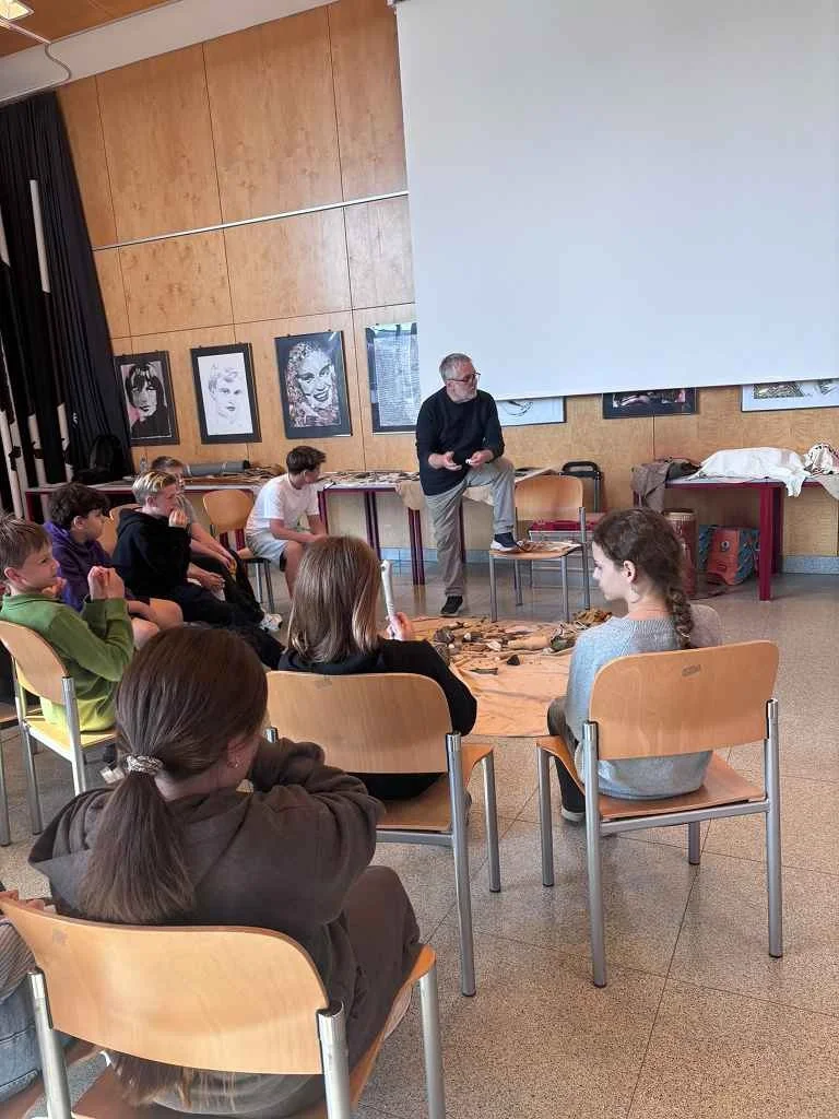 Älterer Mann erklärt Schülern Museumsobjekte in einem Klassenzimmer in Österreich
