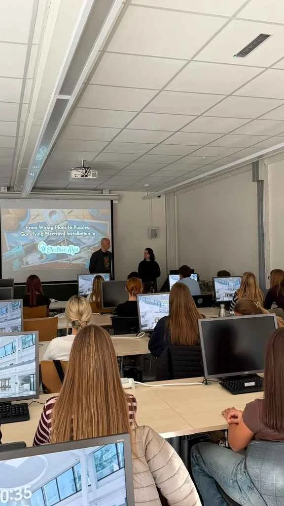 Vortragende präsentieren "Electric Alps" in einem Schulungsraum mit Studierenden vor Computern.
